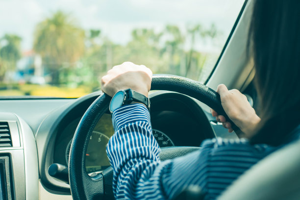 在路上开车时，一个女商人的手在方向盘上。在路上开车时，女人的手集中在方向盘上。查看和女性的手在方向盘上。图片下载