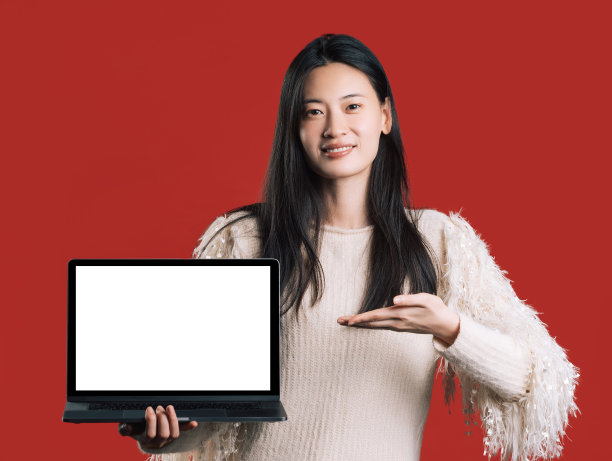 红色背景上的演播室里穿着浅色套衫的亚洲年轻女性。概念与笔记本电脑。设计的位置图片下载