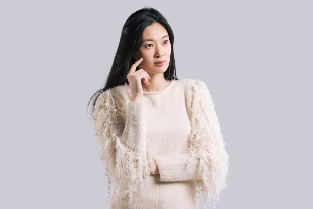 在灰色背景下的演播室里，亚洲年轻女性穿着浅色套头衫图片下载