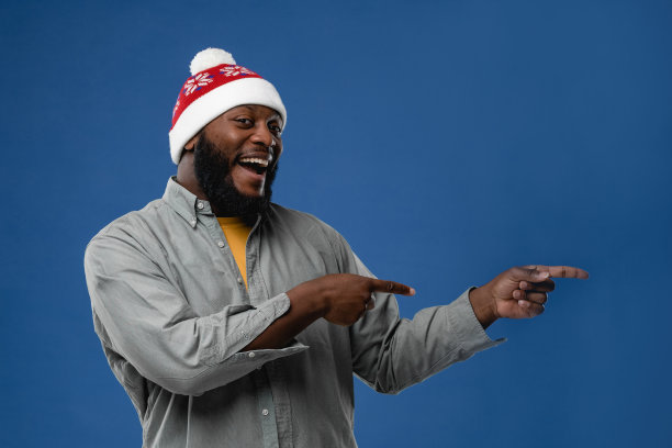 戴着圣诞帽的非裔美国年轻人的肖像。概念照片在工作室的彩色背景图片下载