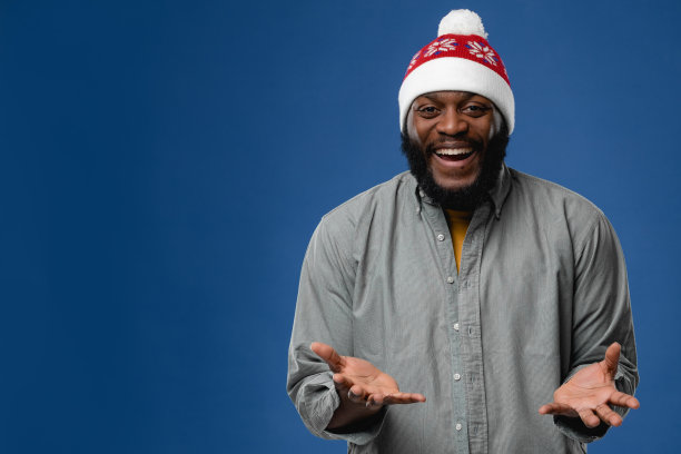 戴着圣诞帽的非裔美国年轻人的肖像。概念照片在工作室的彩色背景图片下载