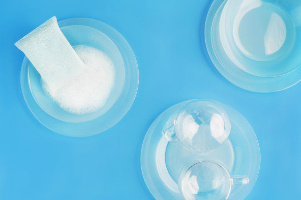 抽象时尚的蓝色背景与美丽的浅蓝色玻璃盘子，杯子，清洁海绵和肥皂泡。家务的概念。模型为您的设计。平的风格。图片下载