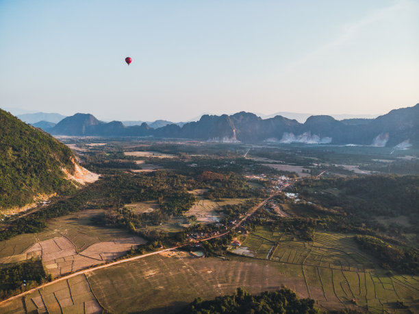 条纹热气球飞过大地，傍晚的风景和城市的小房子，老挝的一条河万荣。老挝。图片下载