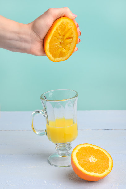 创意时尚的照片，色彩柔和。女用手捏碎橙汁。垂直的框架。美味的果汁和草莓的心情。图片下载