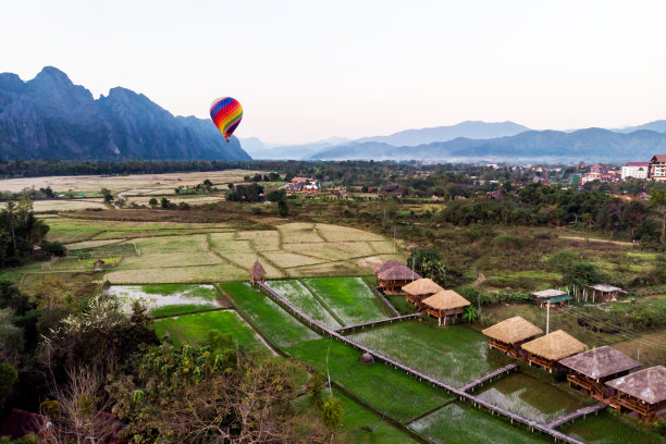 条纹热气球飞过大地，傍晚的风景和城市的小房子，老挝的一条河万荣。老挝。图片下载