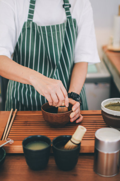 日式茶道，抹茶用竹打蛋棒准备，平铺抹茶拿铁准备理念。在咖啡工具的背景上，将绿色粉末混合在一个马克杯里制作抹茶。图片下载