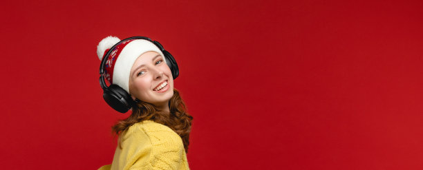 红色背景的演播室里穿着黄色毛衣戴着圣诞帽的漂亮年轻女人。戴着耳机图片图片下载