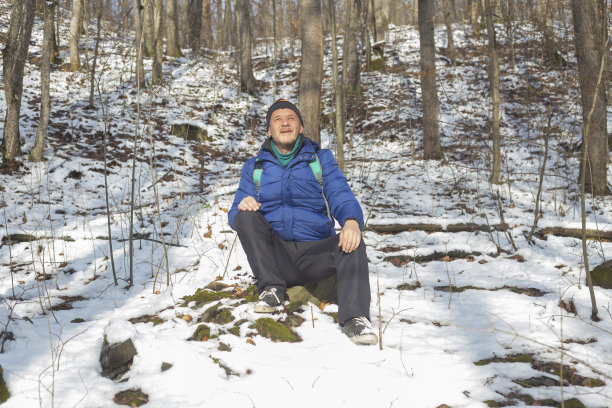 快乐的成年人徒步旅行者坐在岩石上，享受阳光在雪山森林图片下载