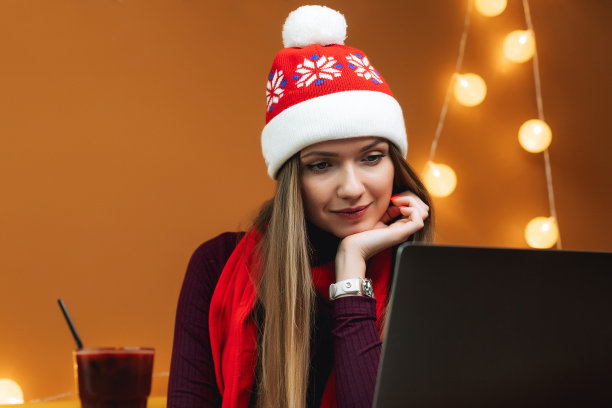 圣诞和新年心情。年轻漂亮的女孩戴着圣诞帽，用笔记本电脑工作或放松图片下载