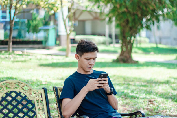 亚洲男人在公园里用智能手机图片下载