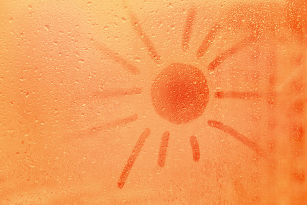 手绘橙色形状的太阳文字在泥泞冰冷的玻璃潮湿的窗户在城市日落图片下载
