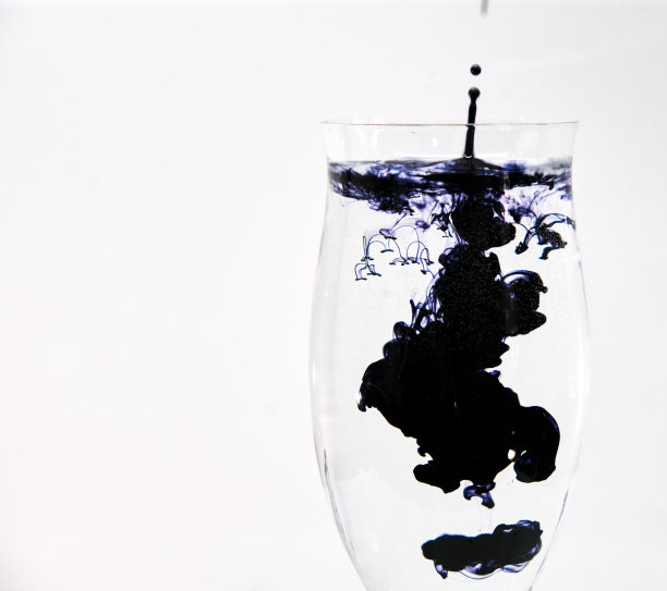 蓝色和黑色的墨水滴进酒杯里的水图片下载