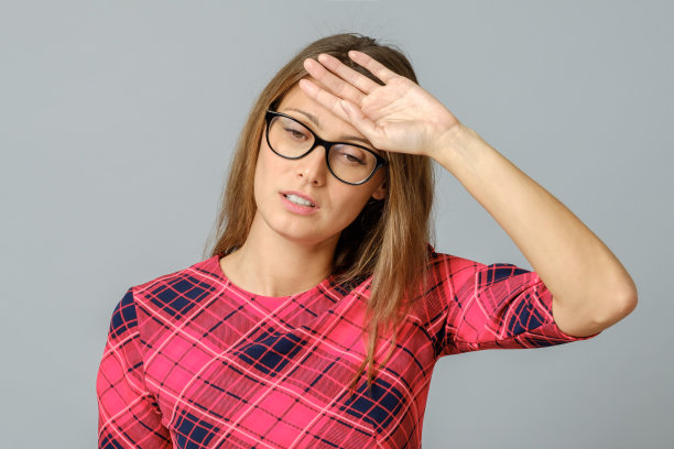 美丽的女人总是把手放在头上，看起来很紧张，又累又沮丧。灰色背景图片下载