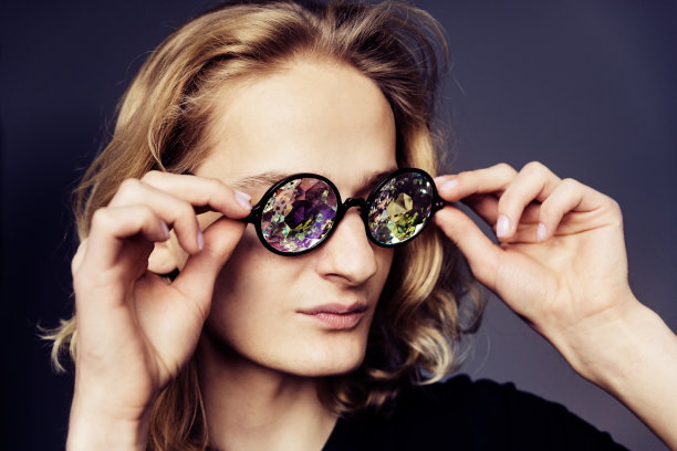 年轻英俊的小伙子，金色长发，黑色t恤，灰色背景，眼镜万花筒。图片下载