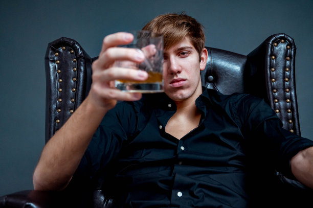 肖像年轻男子坐在一个棕色的皮革扶手椅在工作室和持有一个饮用玻璃库存照片图片下载