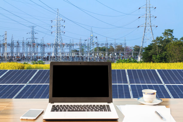 原型图像的笔记本电脑与黑屏，智能手机，咖啡杯在木制桌子上的太阳能电池板在蓝天背景的高压塔，替代能源概念，清洁能源，绿色能源。图片下载