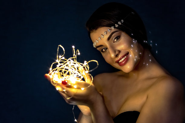 一个黑发的女孩，在蓝色背景的夜晚，手里拿着火花，甜蜜地微笑着。图片下载