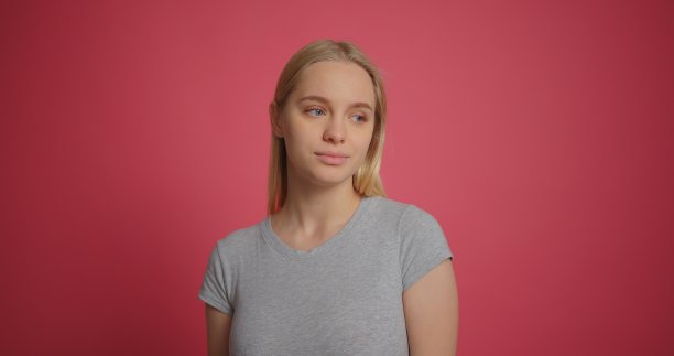 金发女孩在灰色t恤看着相机在粉红墙背景慢动作图片下载