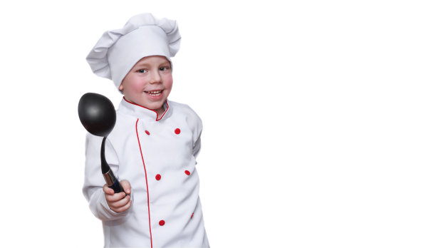 一个带着帽子的有趣的孩子，笑得很有趣，拿着勺子拿着勺子，看着镜头。餐厅或咖啡馆的概念，烹饪菜单。本空间图片下载