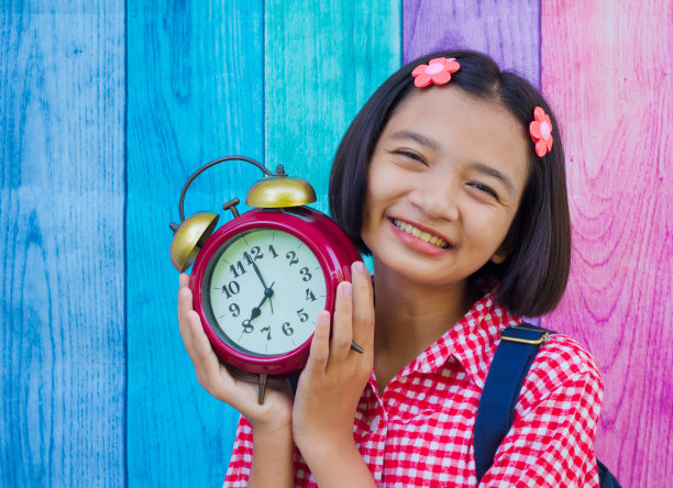 亚洲小女孩手持彩色背景的闹钟。图片下载