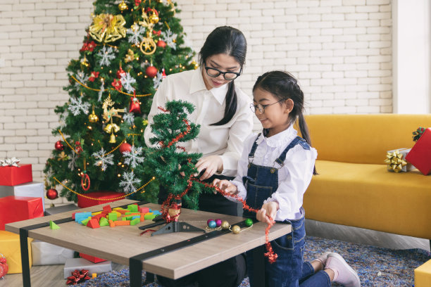 快乐的妈妈和女儿在家里的圣诞树上放礼物。图片下载