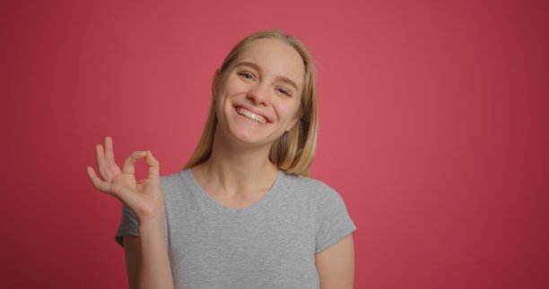 快乐的金发女孩微笑着，并在粉红色的墙上显示ok手势图片下载