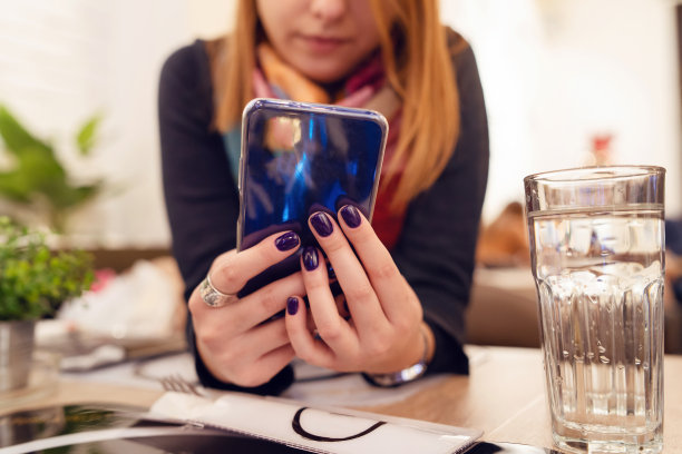靠近女性的手年轻的未知女子使用智能手机在餐厅中间的桌子旁图片下载