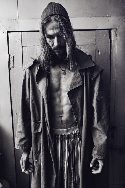 年轻的白人农村男子穿着一件织物雨衣站在一个农村的房子里。图片下载