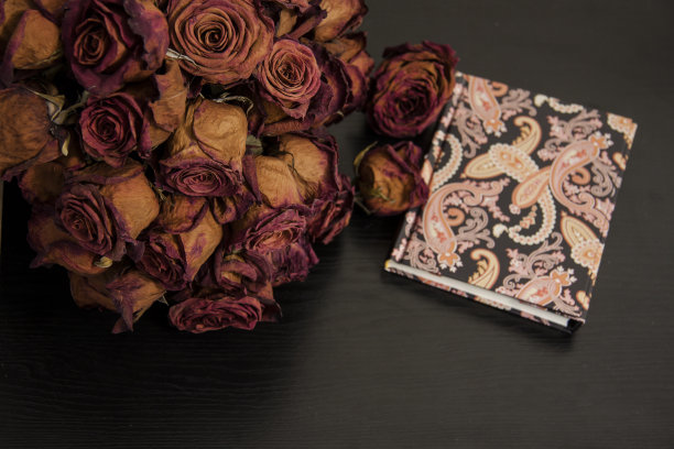 黑色背景上的浪漫复古构图。红干玫瑰花和笔记本。图片下载