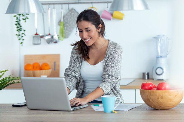 年轻漂亮的女人在厨房里用笔记本电脑和文件工作。图片下载