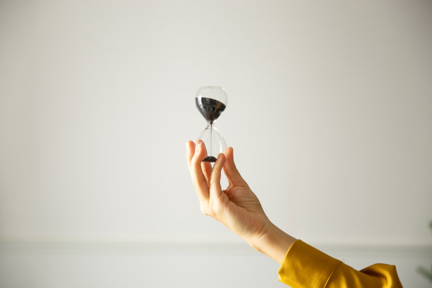 在白色的背景下，一个女性的手拿着一个计时器或沙漏。图片下载