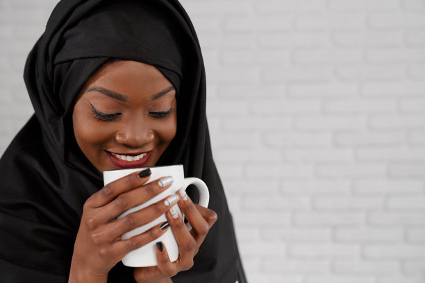 非洲穆斯林妇女在黑色的头巾，拿着杯子，微笑。图片下载