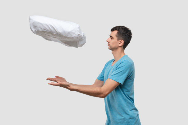 一个穿着蓝色t恤的漂亮的深色头发男人用魔法让枕头漂浮起来。图片下载