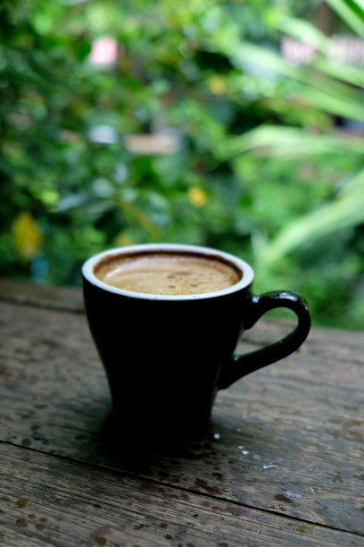 热咖啡杯放在木桌上，以花园为自然背景，清晨雨天的种植园背景——意象图片下载