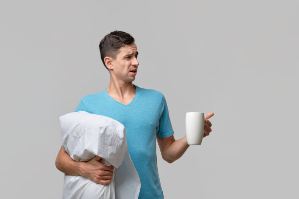 年轻的褐发男子一边拿着白色的咖啡，一边拿着白色的枕头，心里充满了怀疑。图片下载