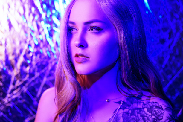 华丽的金色霓虹色，红蓝色，抽象的背景。戴白色镜片的女孩。俱乐部的照片。肩膀上有花纹身的女孩。图片下载
