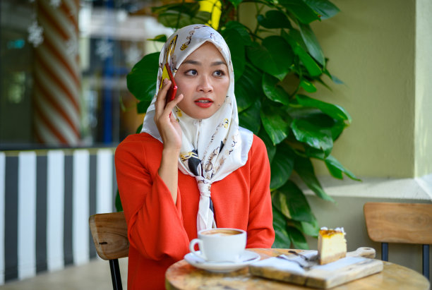 美丽的亚洲穆斯林女人在咖啡馆和她的智能手机图片下载