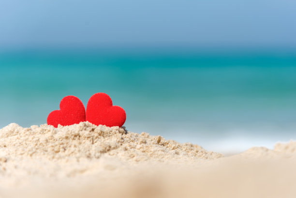 情人节和结婚的概念。两对红心情侣在夏日天堂沙滩上举行婚礼，以蓝色为背景。图片下载