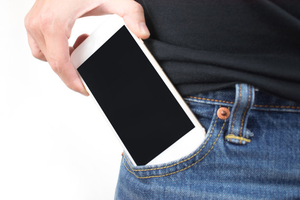年轻的手把智能手机放进牛仔裤口袋的特写。孤立的背景图片下载