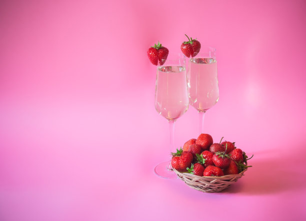 两杯香槟和新鲜草莓柳条篮子在粉红色的背景。图片下载