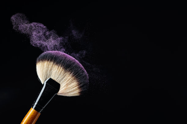 化妆概念与专业的化妆刷与发光的紫色眼影孤立的黑色背景。图片下载