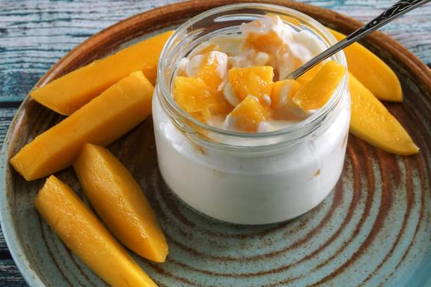 切片的黄色芒果在玻璃透明的罐子与天然酸奶。图片下载