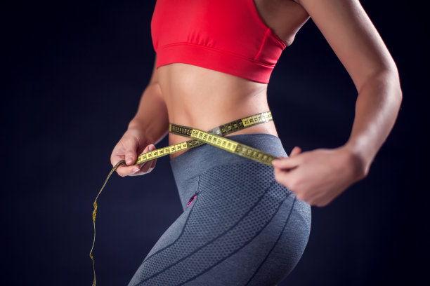 穿红色上衣的妇女用米量腰围。运动与健康概念图片下载