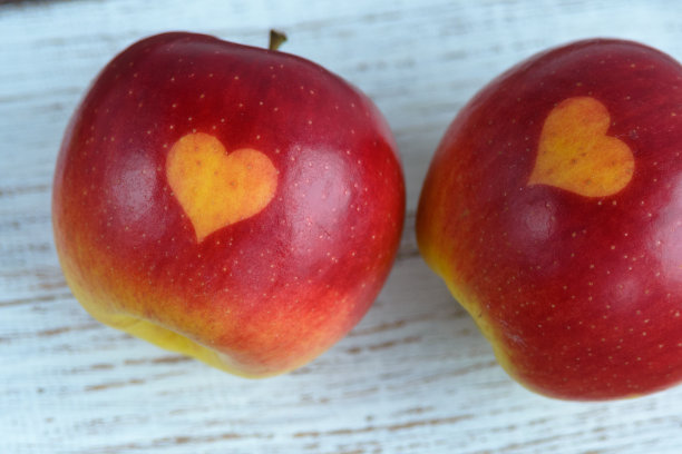桌上放两个红苹果，上面印着心形图案。橙子心在有机水果上。用印刷品种植水果图片下载