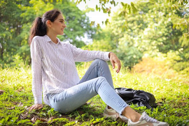 美丽的女人在假期的周末坐在花园里的绿草地上放松。图片下载