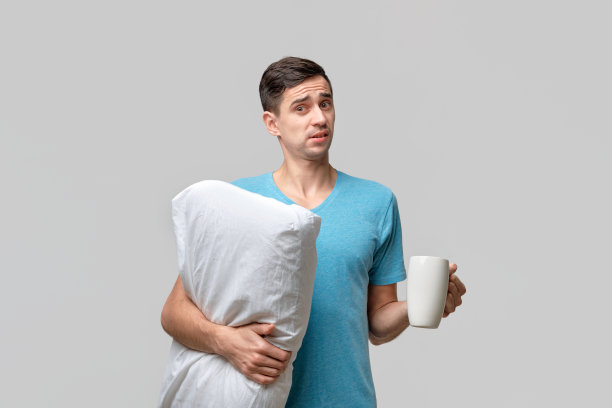 年轻的黑发男子拿着白色的咖啡和白色的枕头图片下载