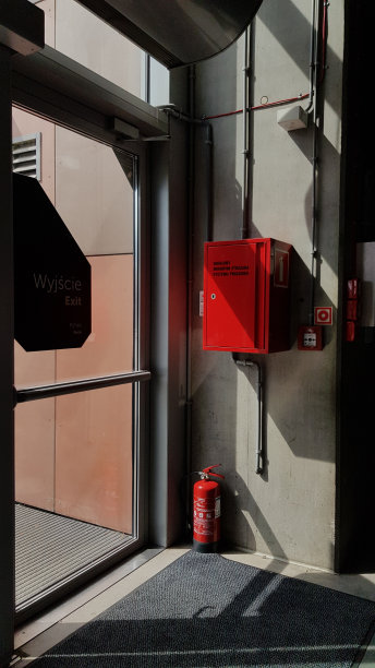 华沙/波兰- 08 22 2019:现代建筑玻璃门出口附近有明亮的红色消防设备和红色灭火器。带有几何阴影和工业纹理的城市抽象。图片下载
