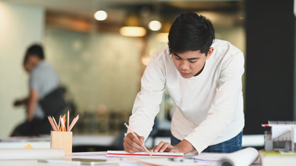 正面照片的年轻建筑师，而他是在工作桌上绘制的建筑计划。图片下载