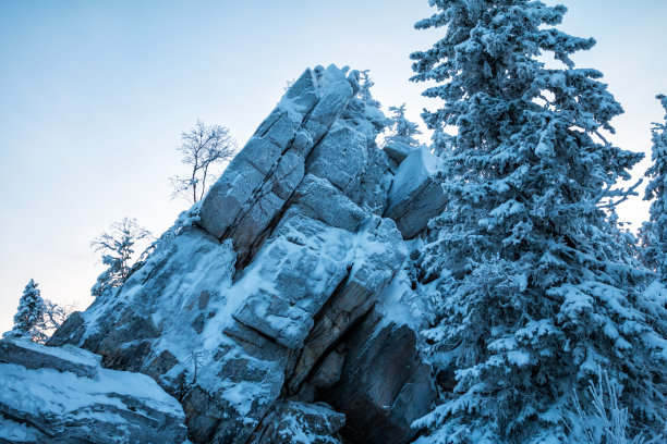 冰雪覆盖的岩石在冬天的森林傍晚的微光中图片下载