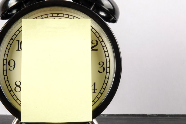 黑色的闹钟贴在木制的表面上，黄色的贴纸贴在白色的上面。图片下载
